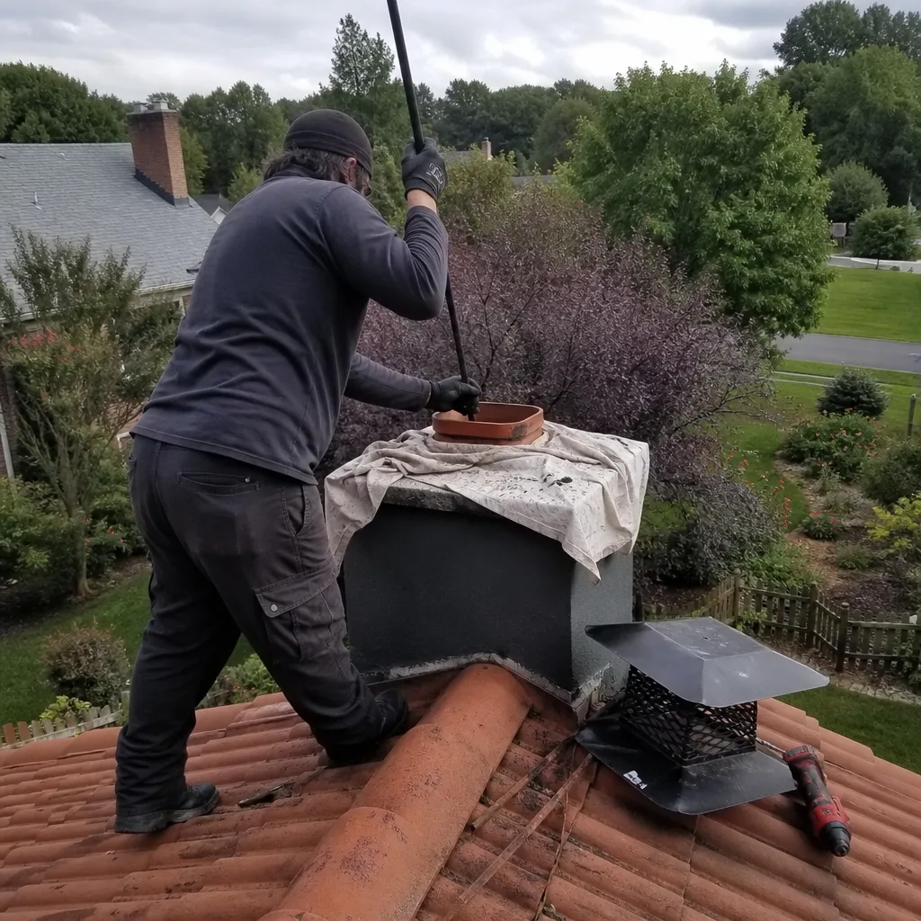 Professional chimney sweep cleaning chimney flue on residential roof
